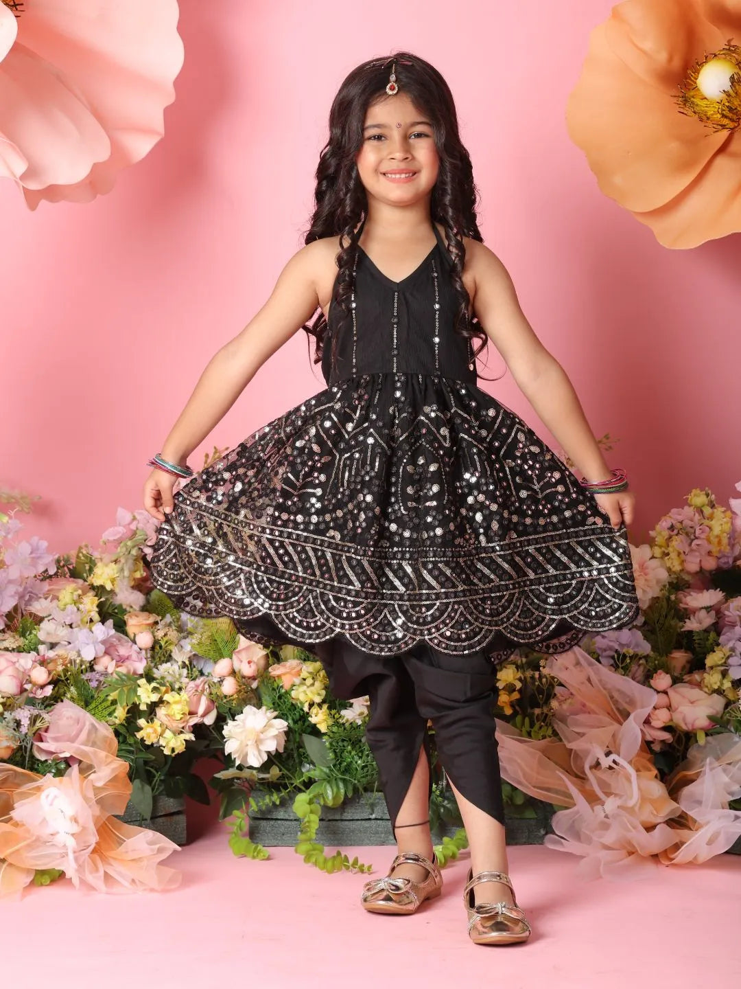 Young girl in a black and silver dress standing in front of pink flowers