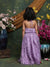 Child in a purple dress standing in front of floral decorations and a decorative wall.