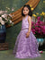 Young girl in a purple dress standing in front of floral decorations.