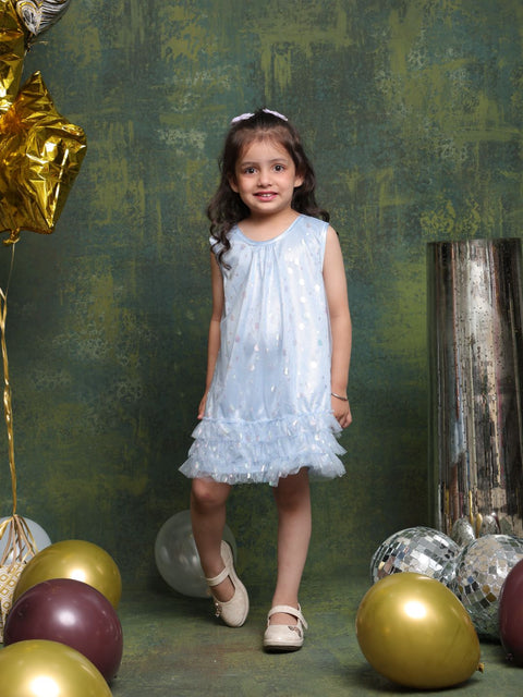 Young girl in a light blue dress standing among colorful balloons against a textured green wall.