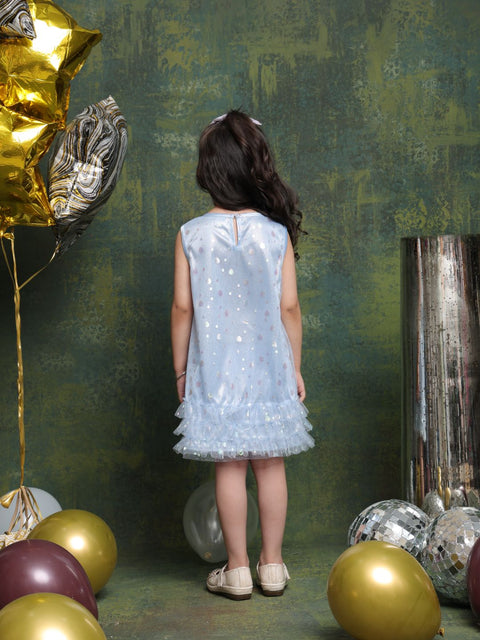 Young girl in a light blue dress standing in front of a textured green wall with gold and silver balloons.