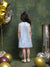 Young girl in a light blue dress standing in front of a textured green wall with gold and silver balloons.