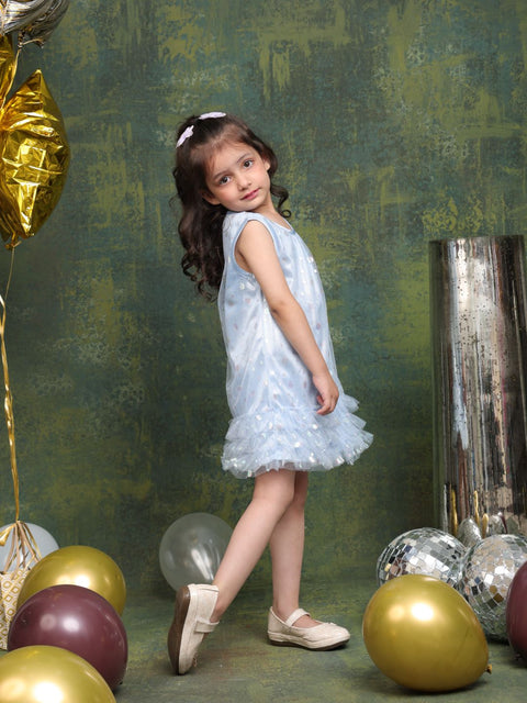Young girl in a light blue dress standing among colorful balloons against a textured green wall.