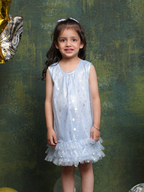 Young girl in a light blue sequin dress standing against a textured green wall.