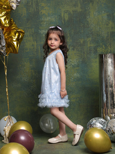 Young girl in a light blue dress standing among balloons against a textured green wall.