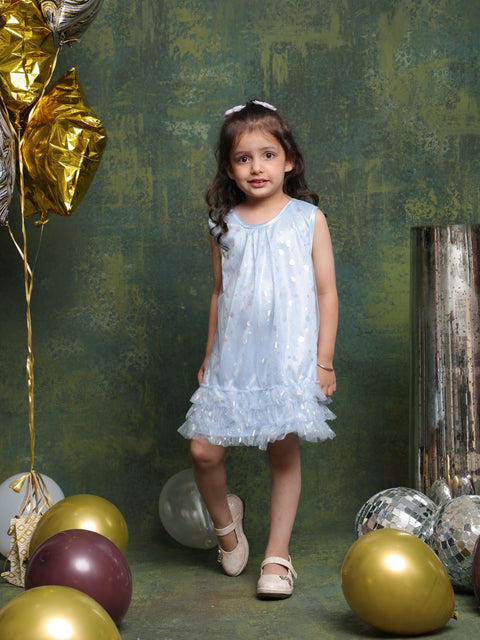 Young girl in a light blue dress standing among colorful balloons against a textured green wall.
