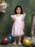 Young girl in a white dress with star patterns standing among colorful balloons against a textured green wall.