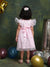 Child in a pink dress standing among balloons against a textured green wall.