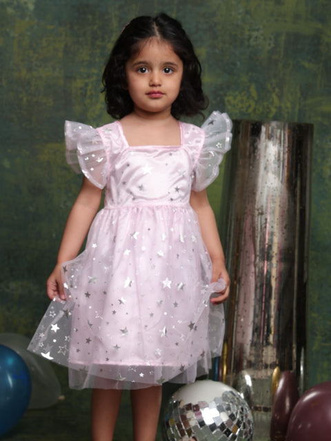 Young girl in a pink dress with star patterns standing against a green wall.