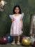Young girl in a pink dress standing among colorful balloons against a textured green wall.