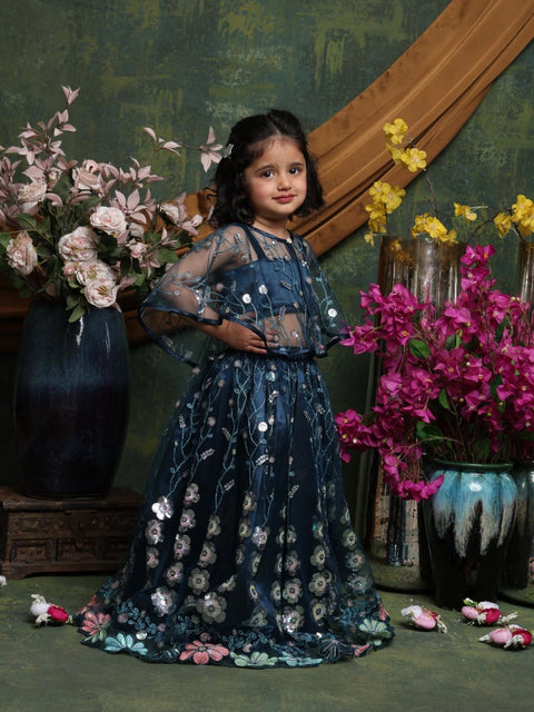 Young girl in a floral dress standing among flowers and decorative elements.