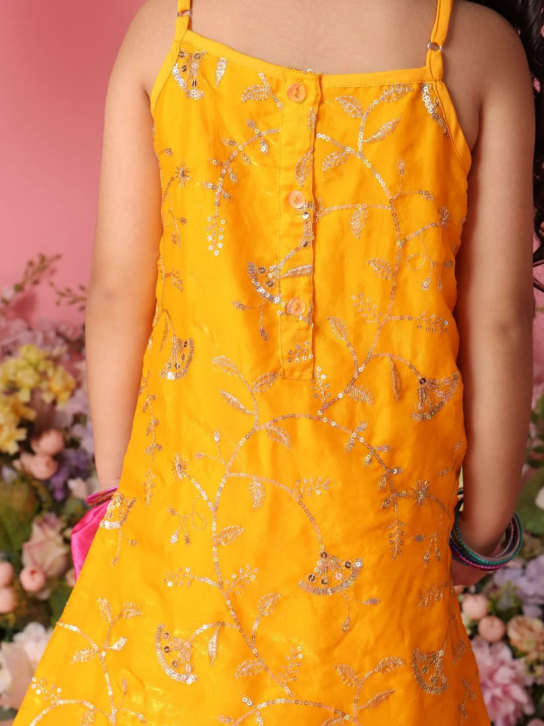 Person wearing a yellow dress with floral patterns against a pink background