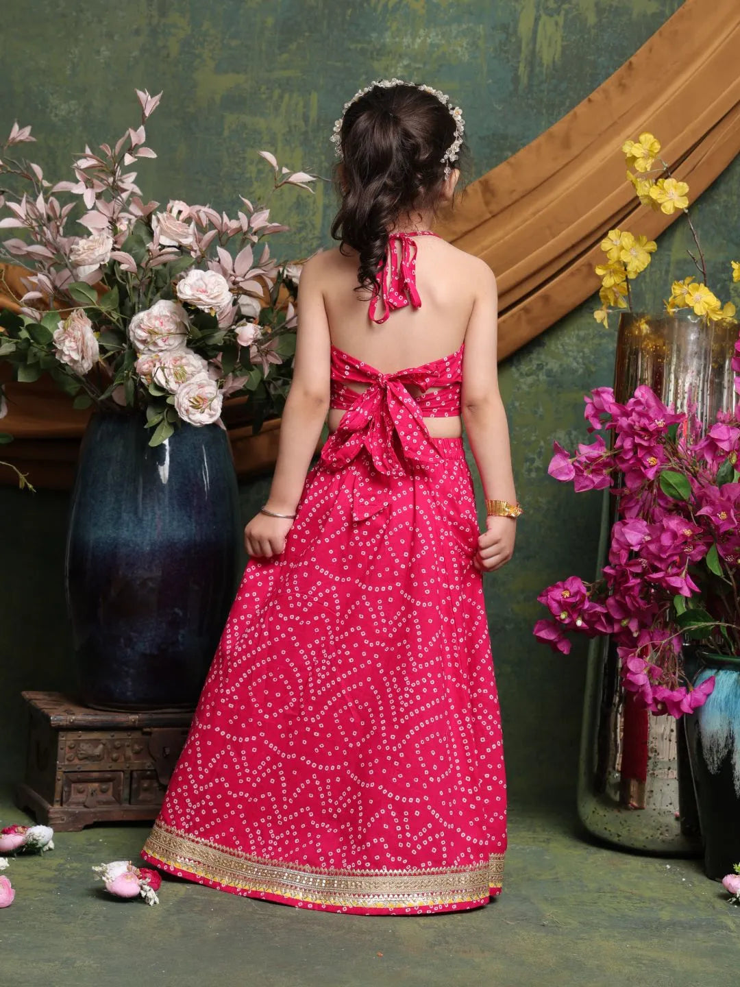 Young girl in a pink traditional outfit standing in front of floral arrangements.