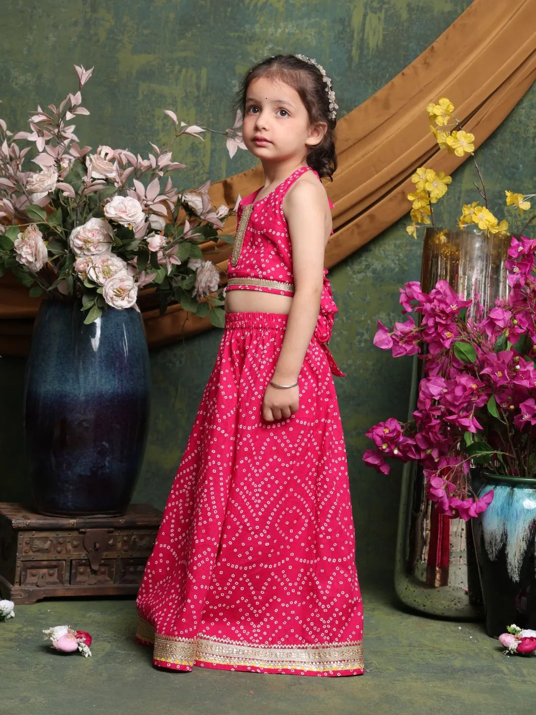 Young girl in a pink traditional outfit standing in front of floral arrangements.