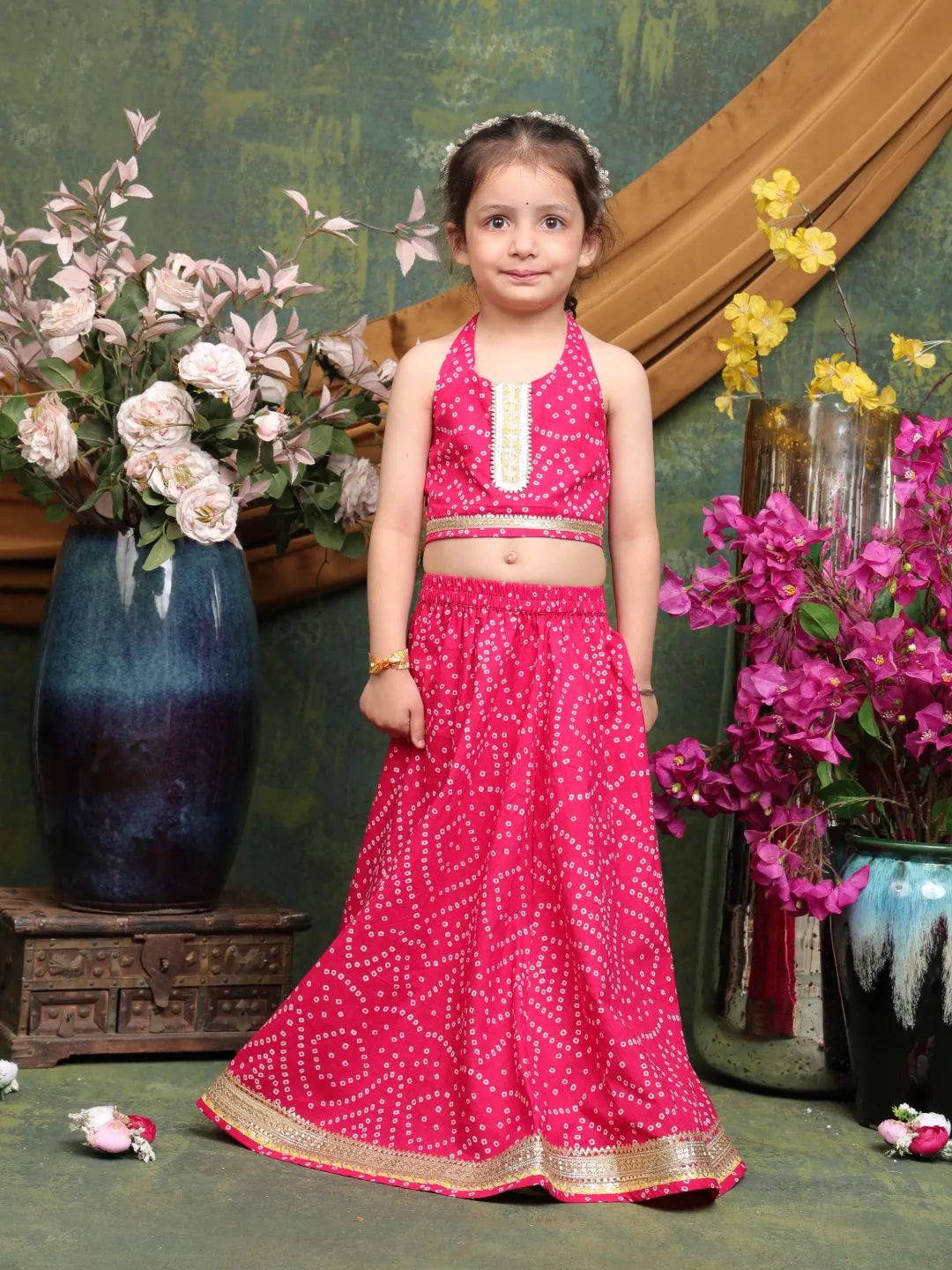 Young girl in a pink traditional outfit standing in front of floral decorations.