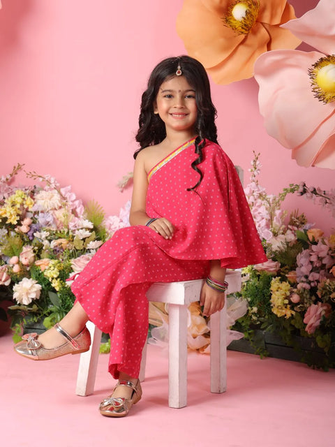 Young girl in a pink traditional outfit sitting on a stool with flowers and decorative elements in the background.