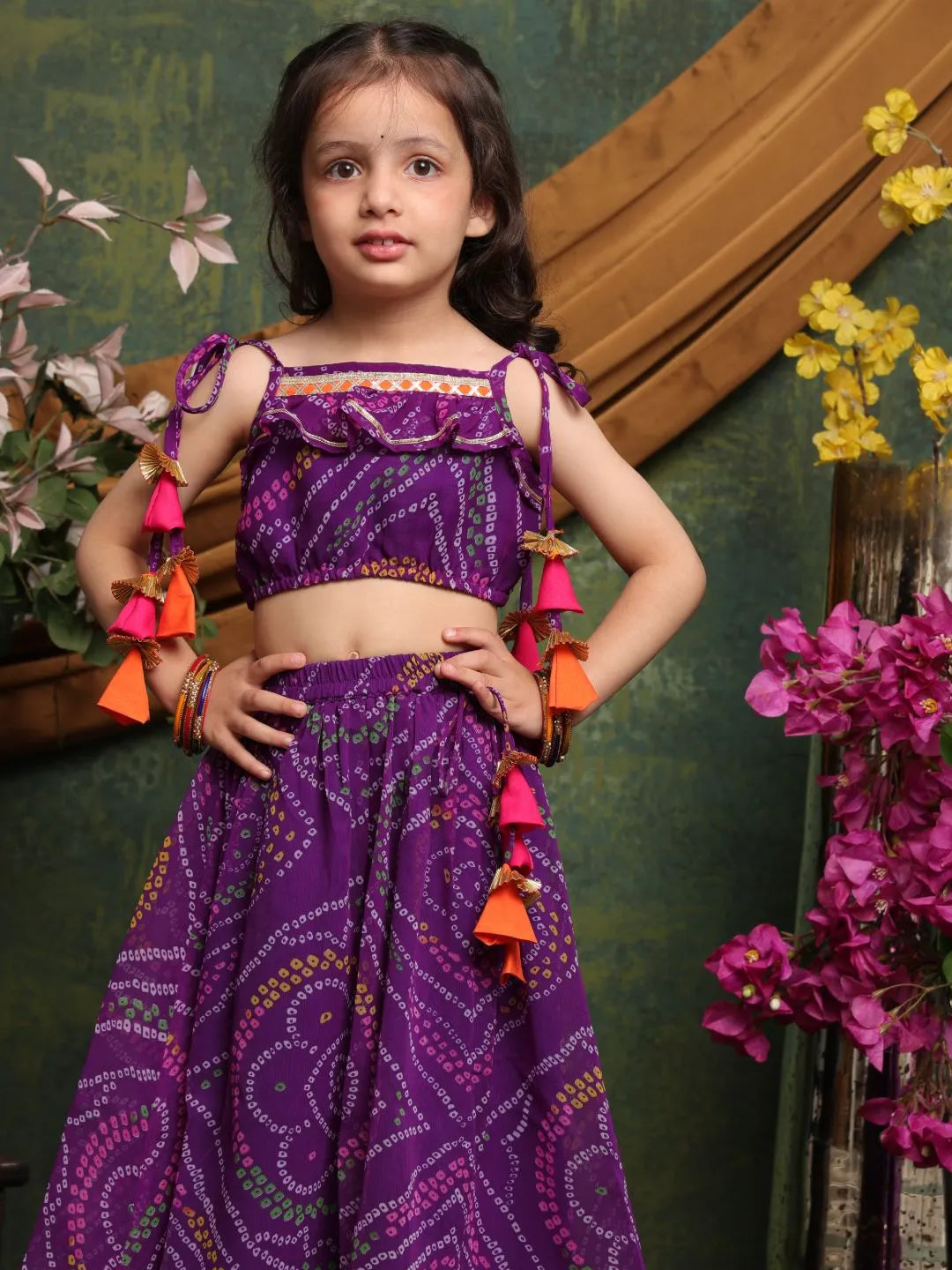 Young girl in a purple traditional outfit with colorful tassels against a decorative background.
