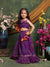 Young girl in a purple traditional outfit standing in front of floral decorations.