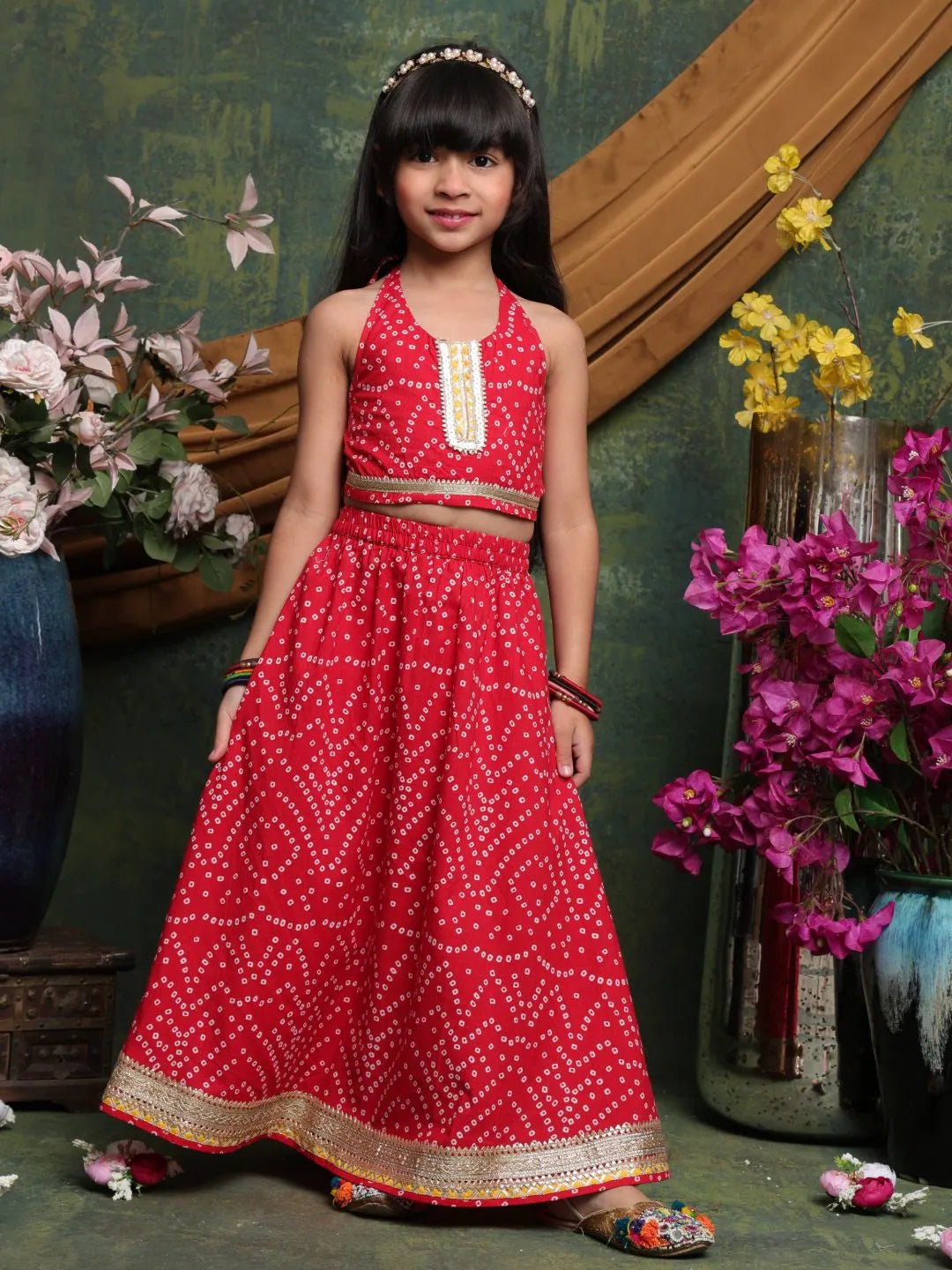 Young girl in a red traditional outfit standing in front of floral decorations.