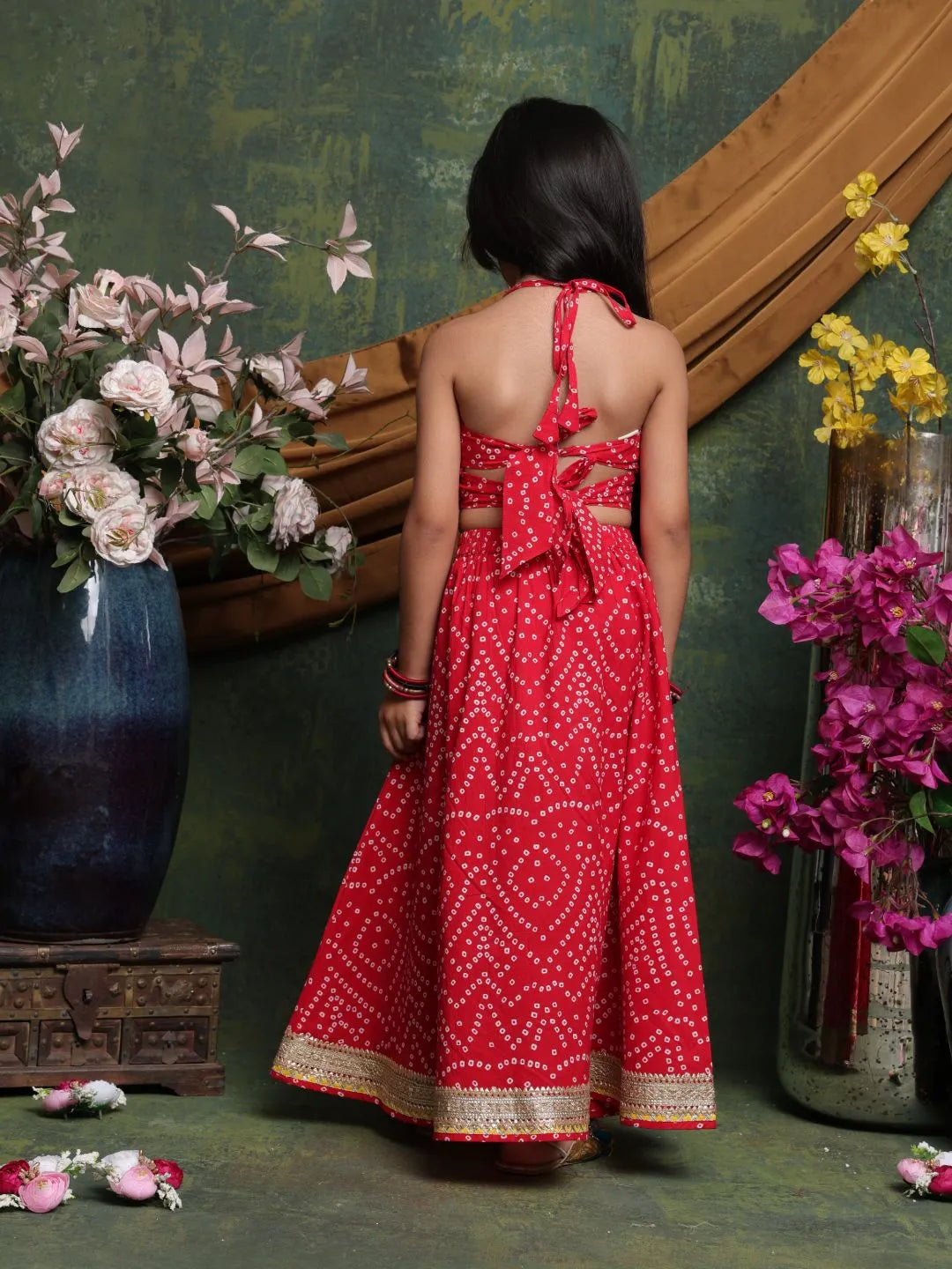 Woman in a red dress standing in front of floral arrangements against a textured wall.