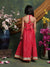 Woman in a red dress standing in front of floral arrangements against a textured wall.