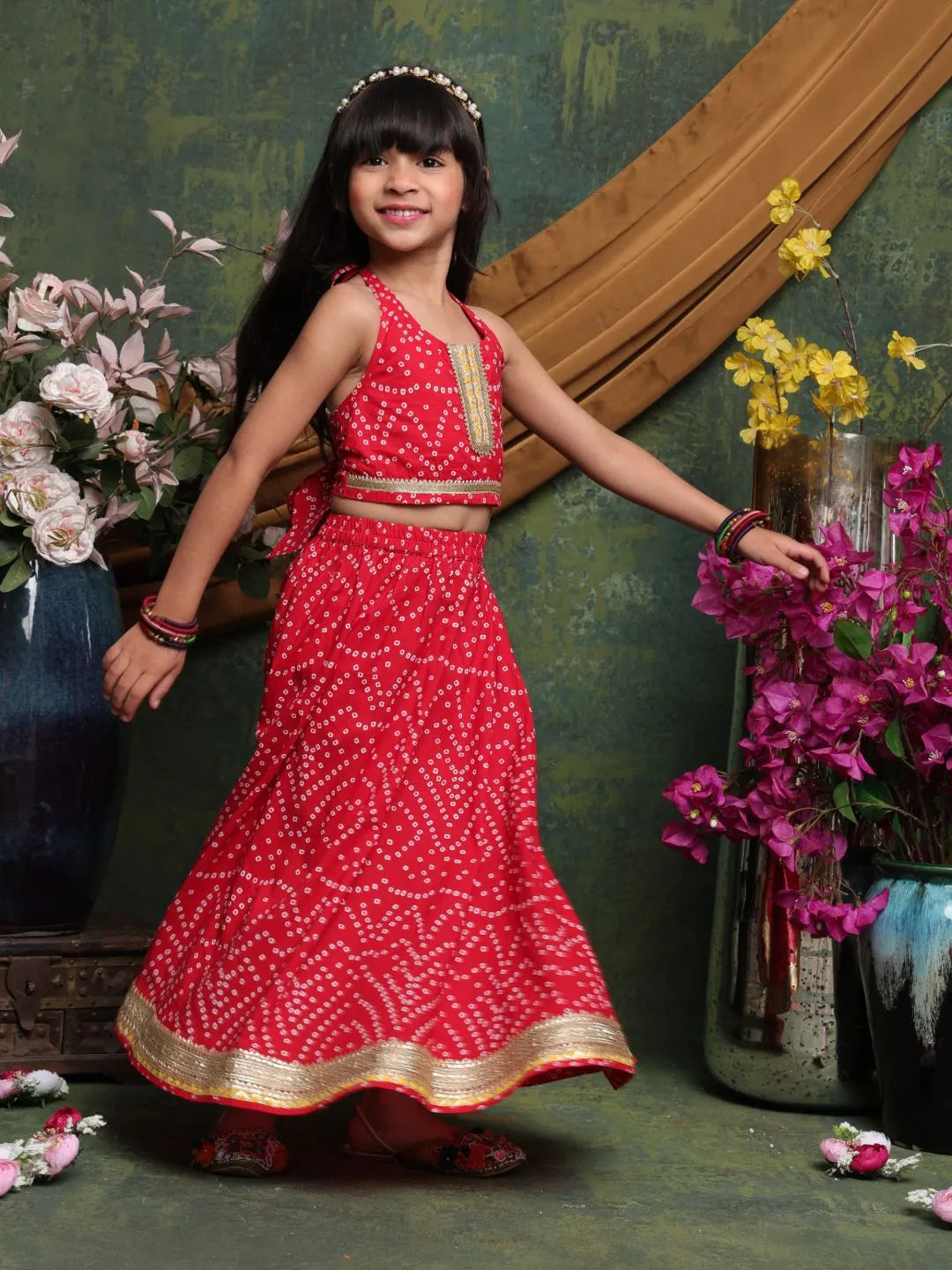 Young girl in a red traditional outfit standing in front of floral decorations.