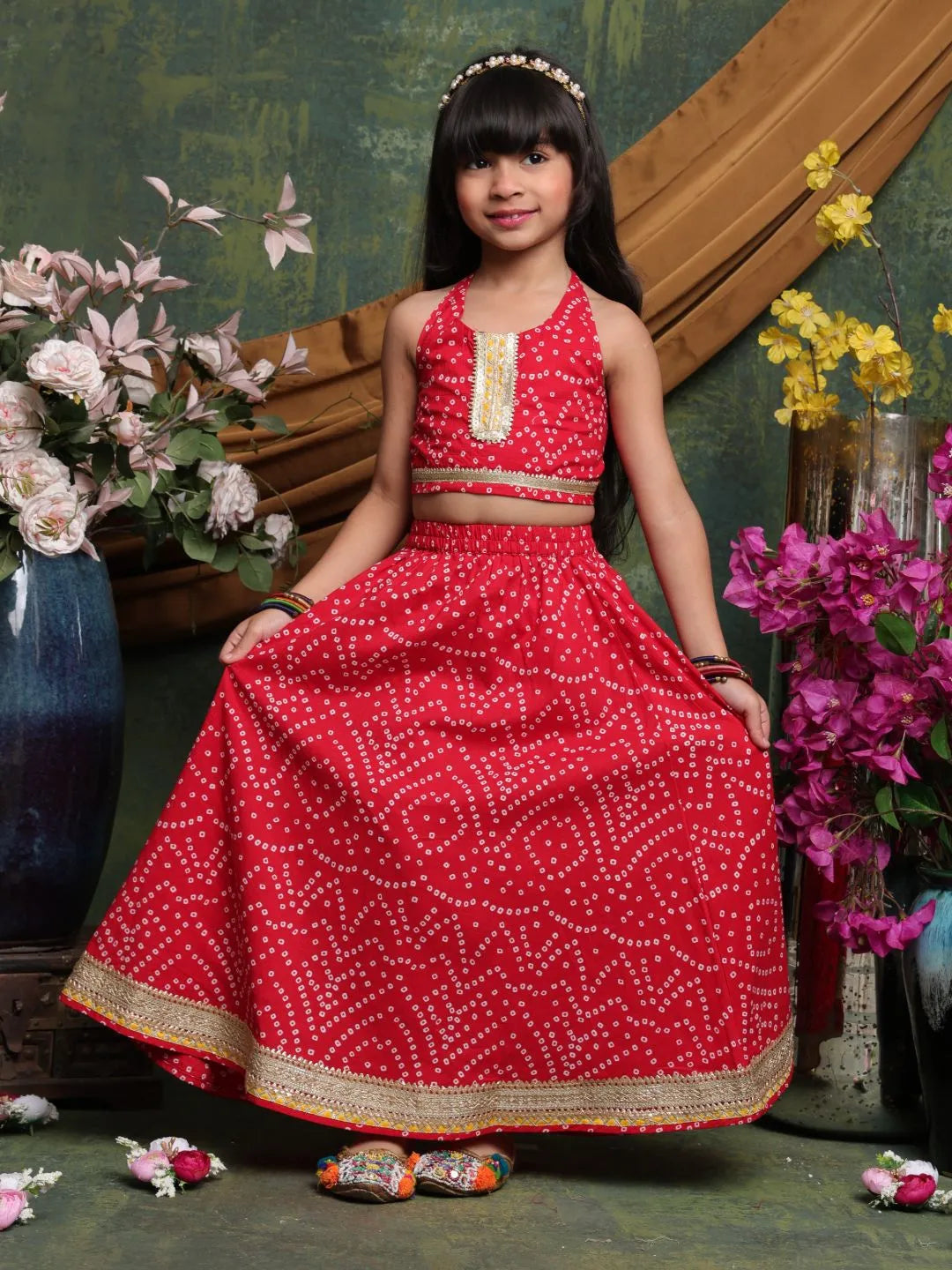 Young girl in a red traditional outfit with floral decorations and a wooden bench in the background.