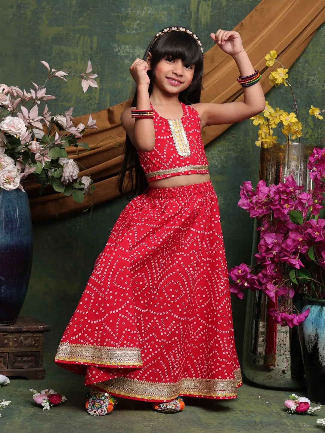 Young girl in a red traditional outfit posing in front of floral decorations.