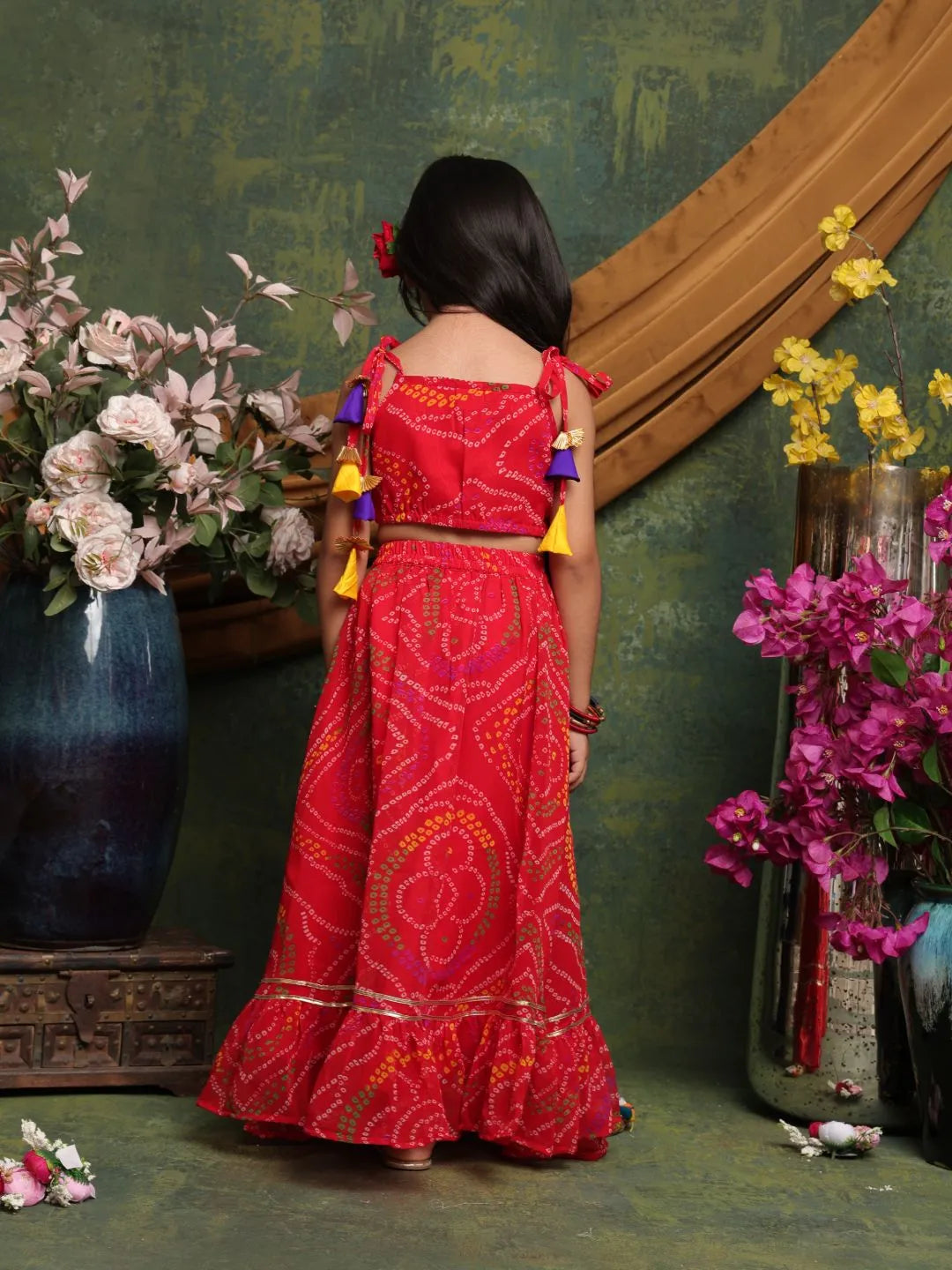 Woman in a red traditional outfit standing in front of a decorative wall with flowers.