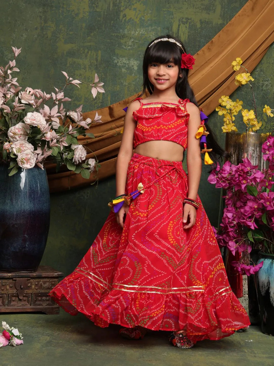 Young girl in a red traditional outfit standing in front of floral decorations.