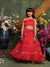 Young girl in a red traditional outfit standing in front of floral decorations.