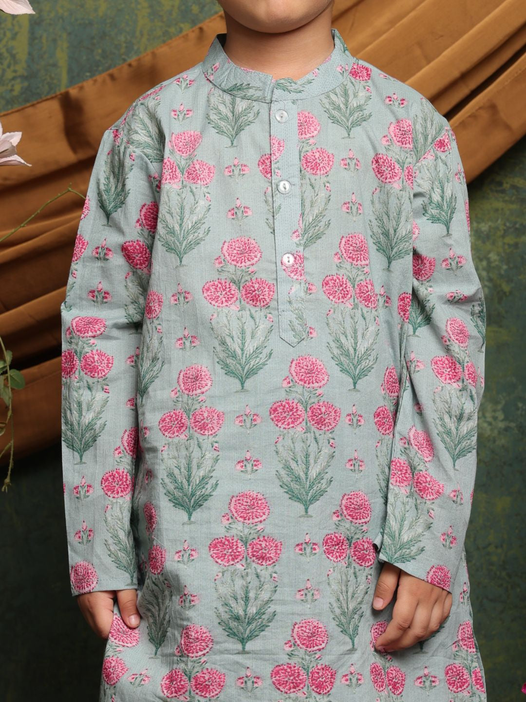Child wearing a floral patterned shirt with pink flowers and green leaves on a light blue background.
