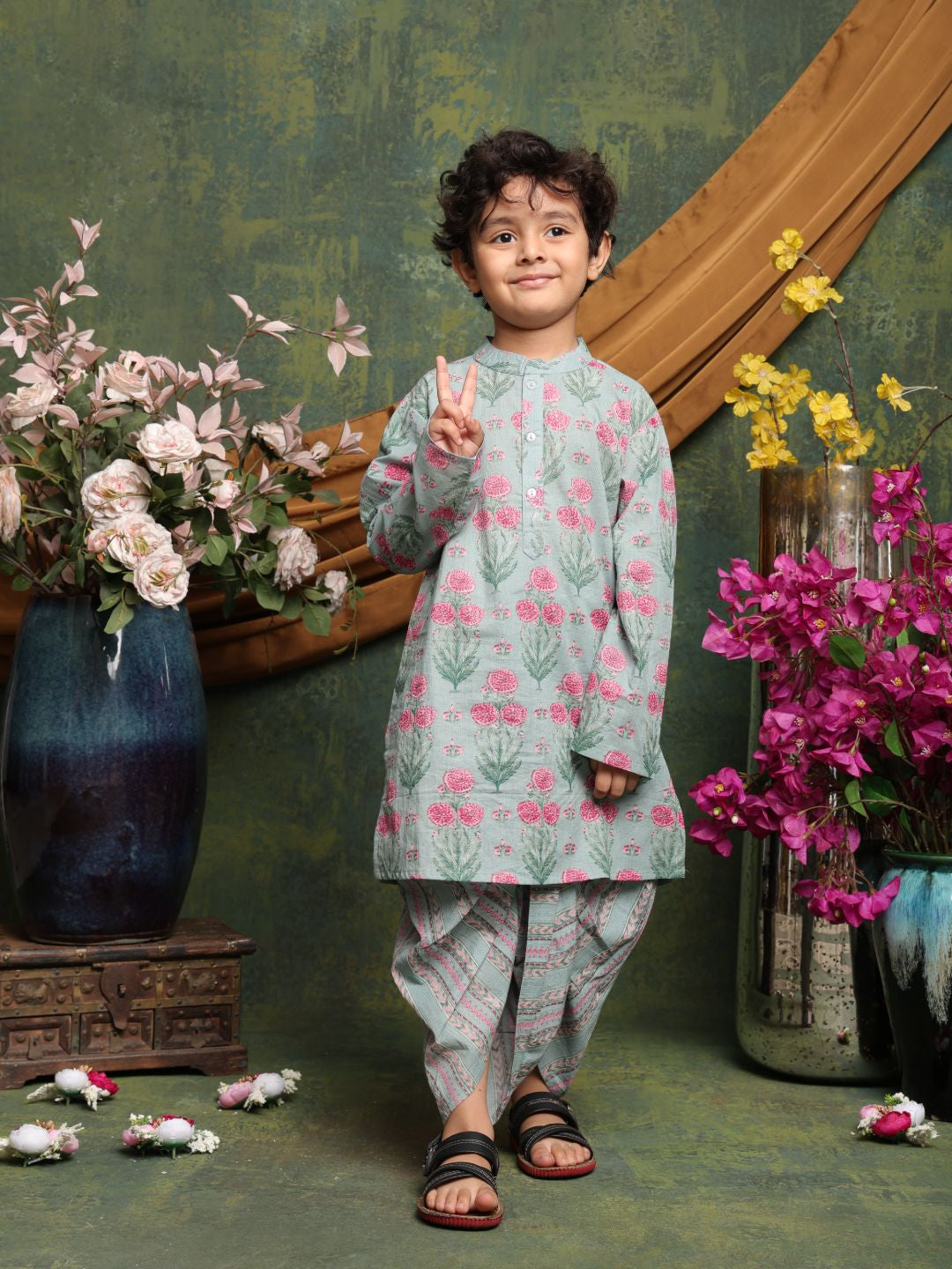 Child in floral traditional outfit standing in front of decorative flowers and a mirror.