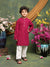 Child wearing a red kurta with white pants standing in front of floral decorations.