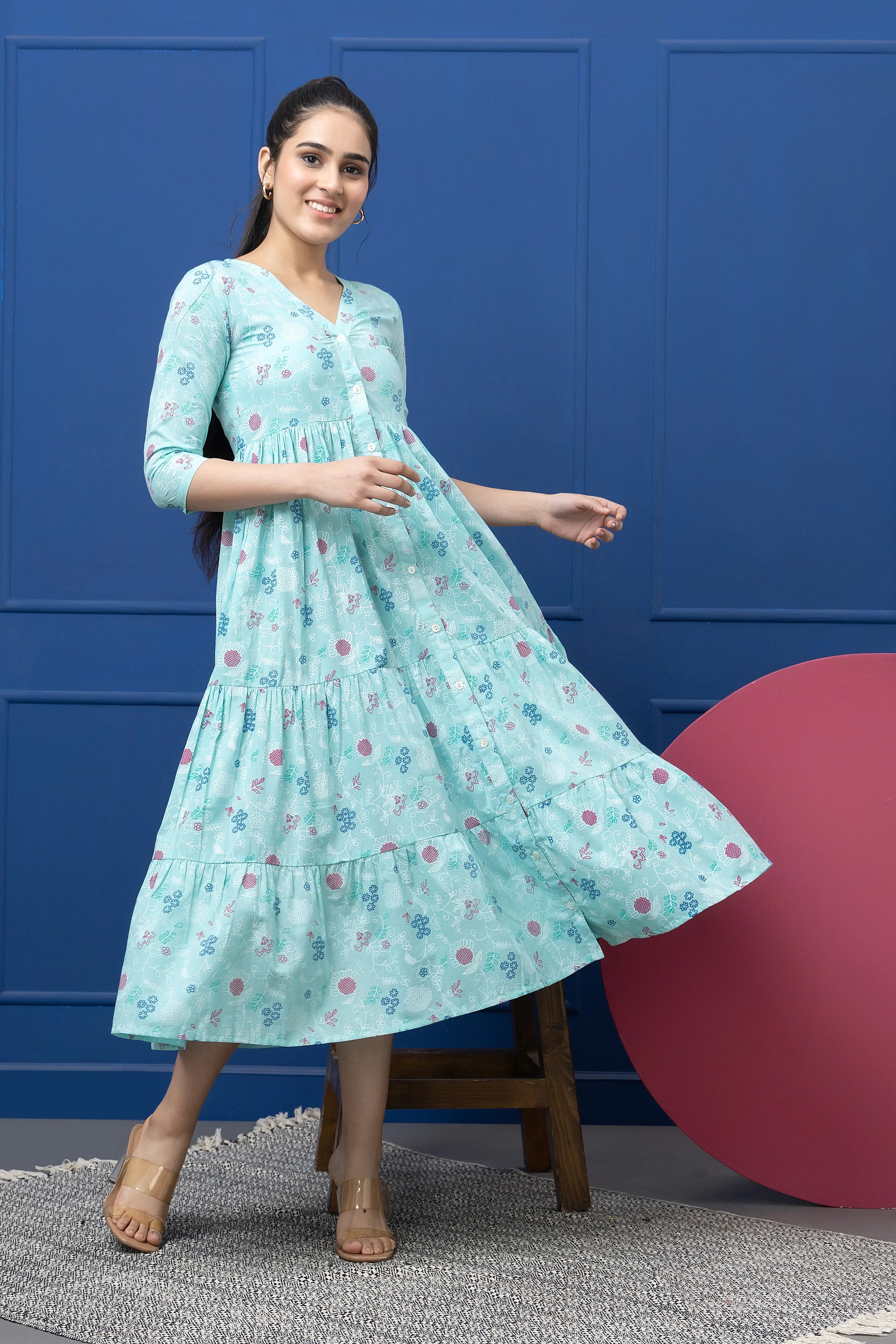 Woman in a light blue floral dress standing against a blue wall with a pink ball on the ground.