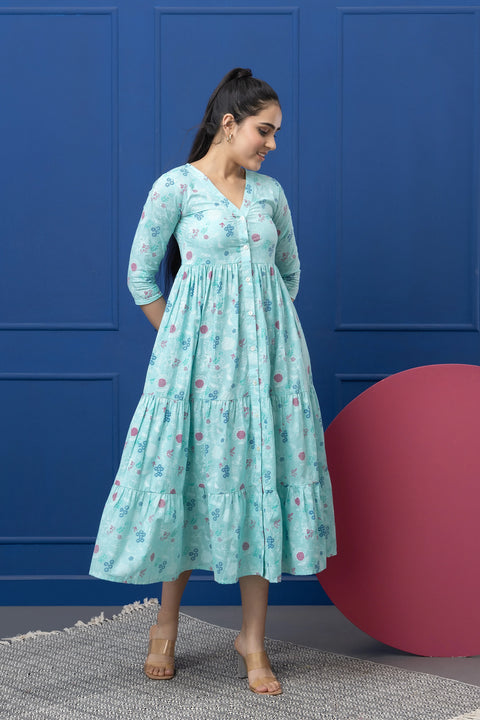 Woman wearing a light blue floral dress against a blue wall with a pink sphere.