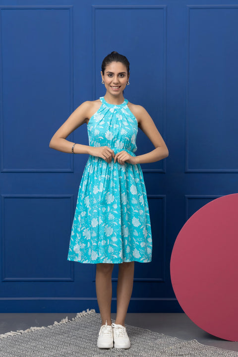 Woman wearing a blue floral dress against a blue wall with a pink circular object.