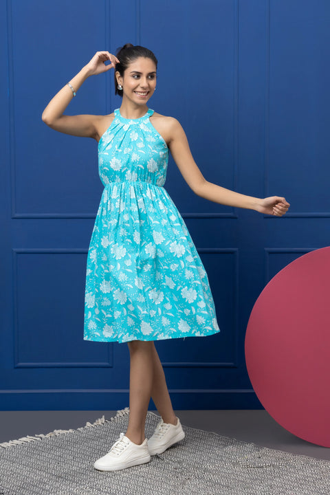 Woman wearing a blue floral dress against a blue wall with a pink object on the floor.