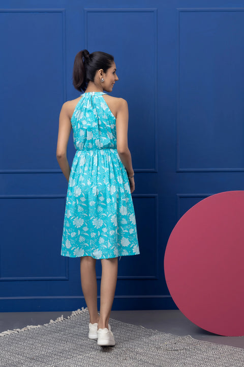 Woman wearing a turquoise floral dress against a blue wall with a pink circular object.