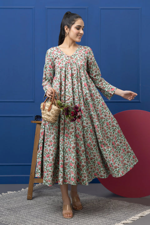 Woman in a floral dress standing next to a stool with a basket against a blue wall.