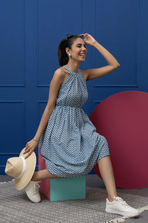 Woman in a blue patterned dress posing against a blue wall with a red circular object.