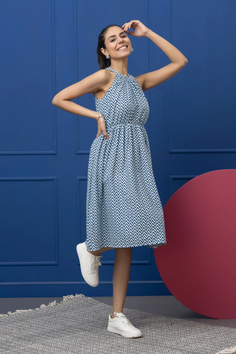 Woman in a blue patterned dress standing against a blue wall with a red ball on the floor.