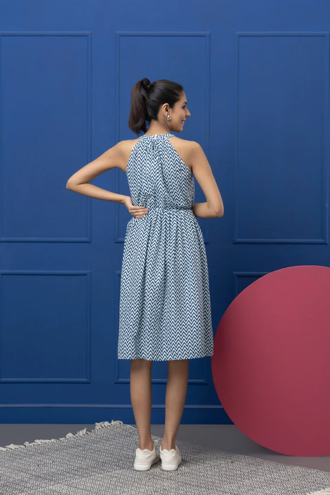 Woman in a blue patterned dress standing against a blue wall with a pink sphere.