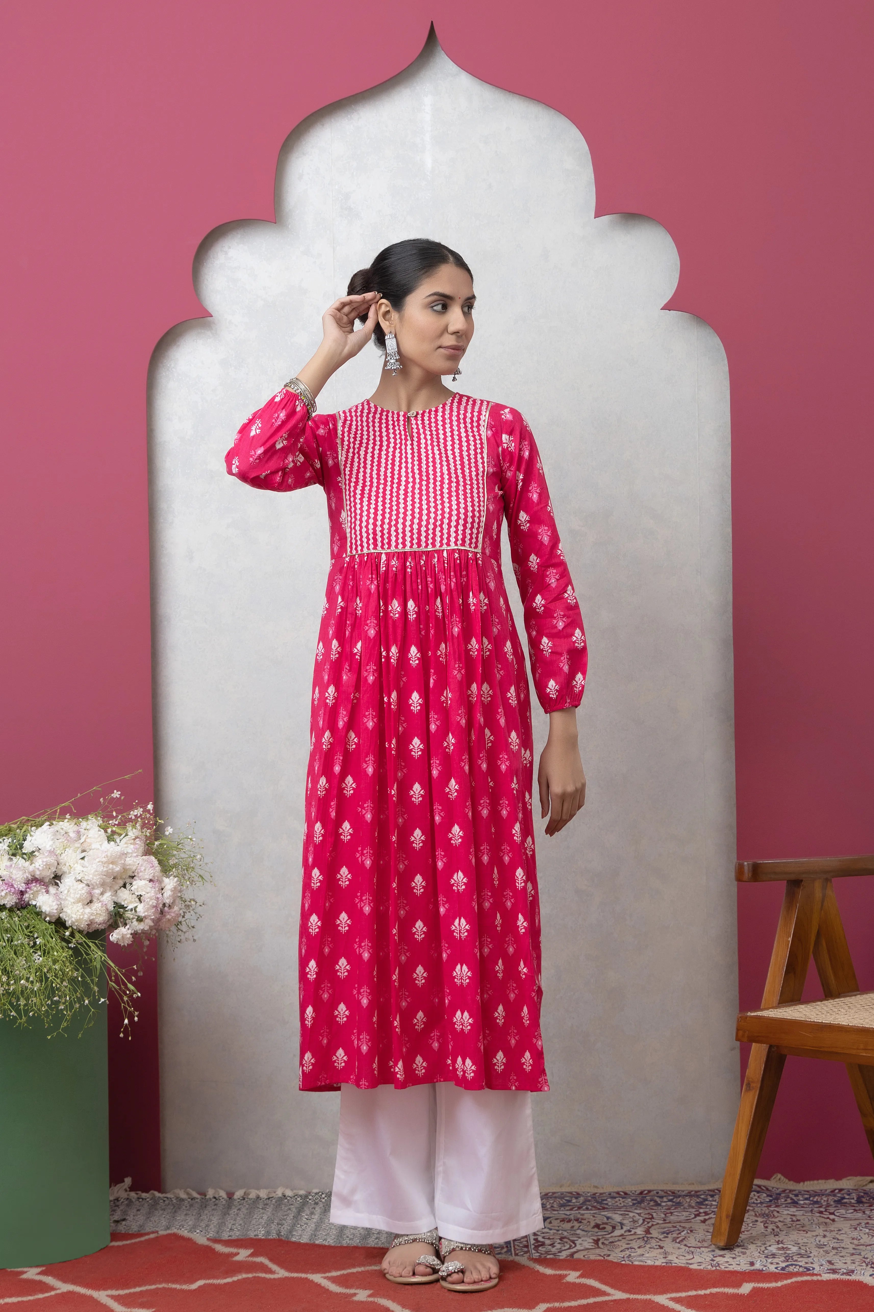 Woman wearing a pink and white patterned dress against a pink wall.