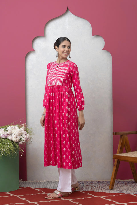 Woman wearing a pink traditional outfit with white patterns against a pink wall.