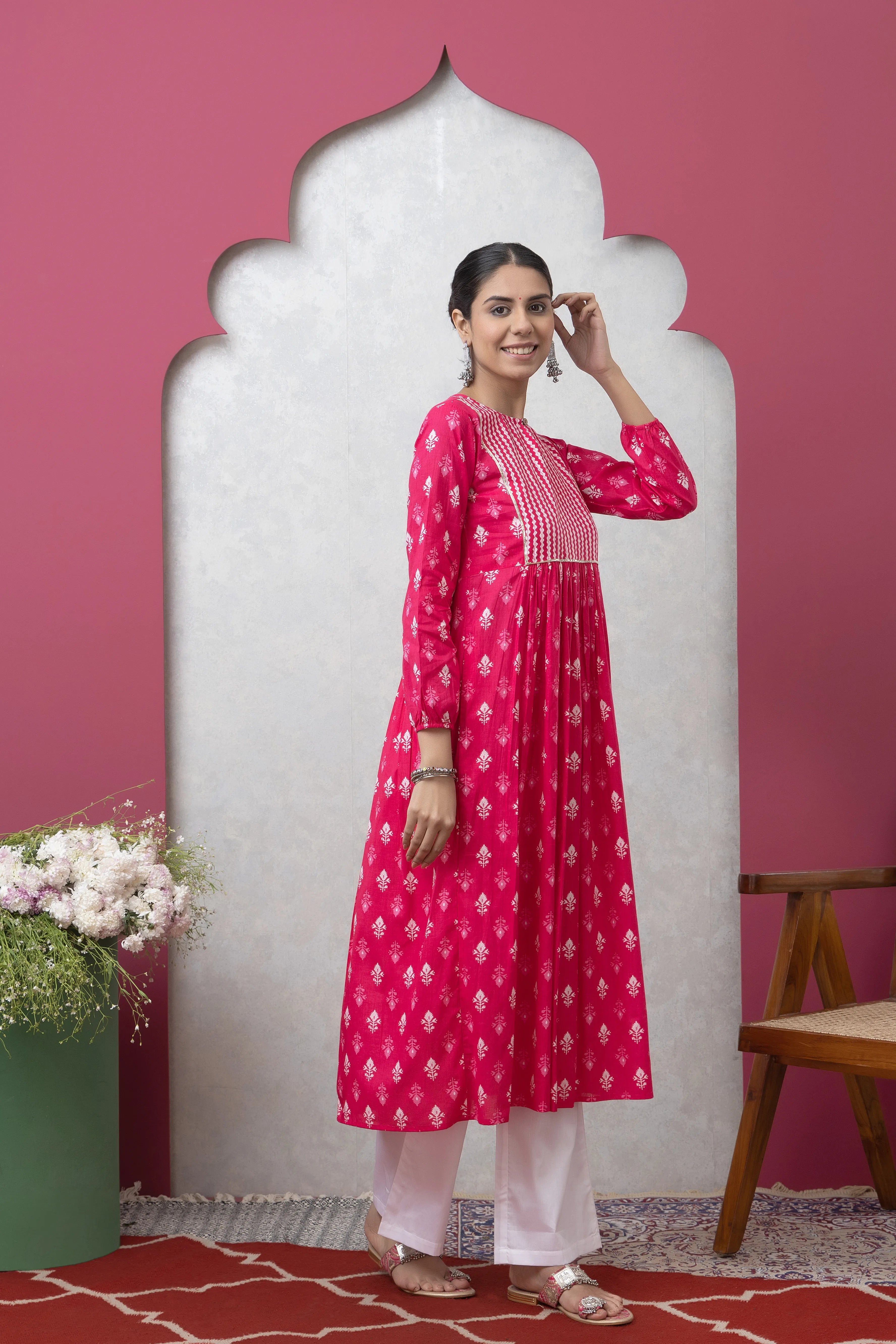 Woman wearing a pink dress with white patterns against a pink wall.