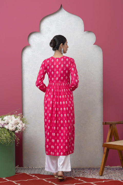 Woman wearing a pink kurta with white patterns against a pink wall.