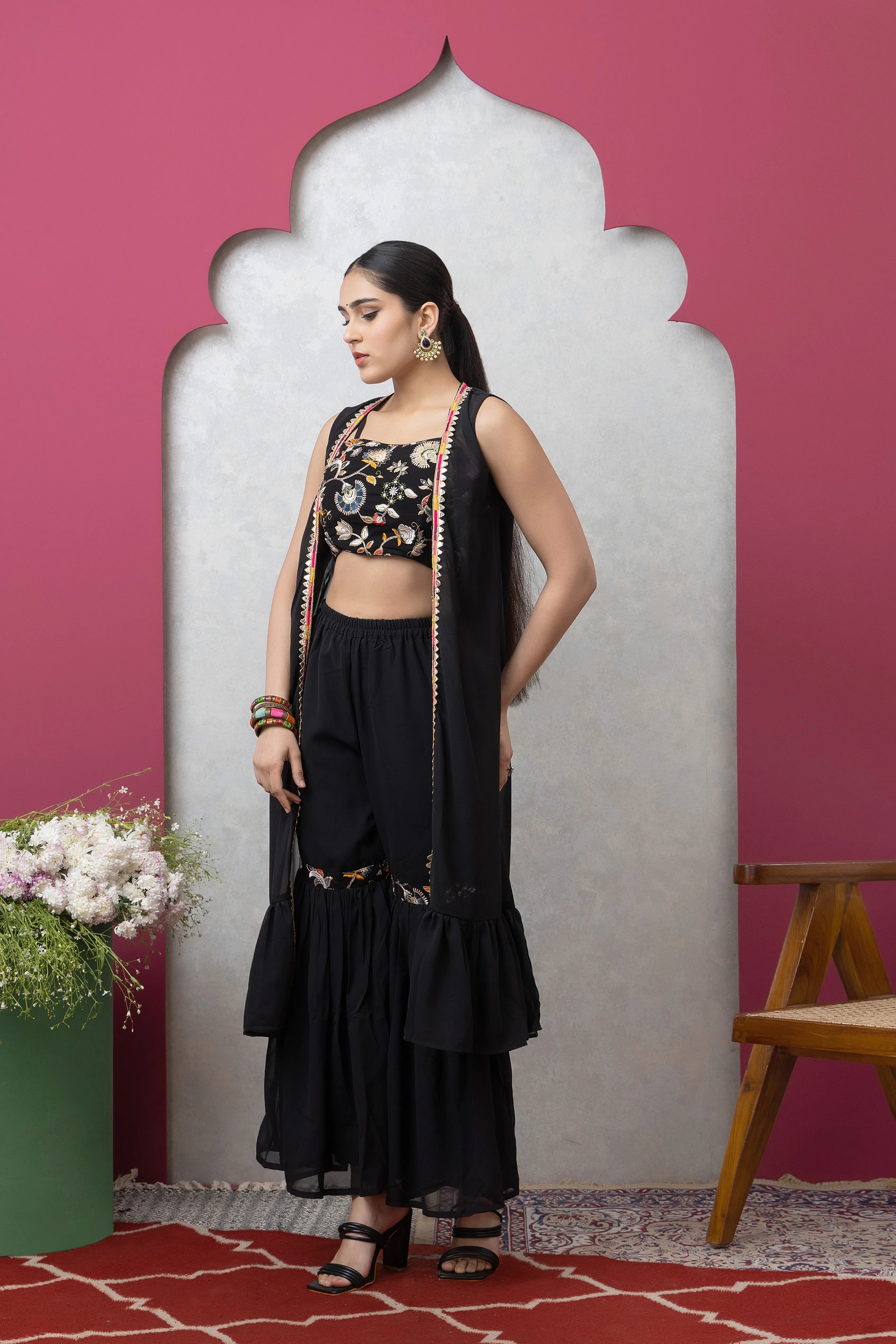 Woman in a black traditional outfit standing against a pink wall with a decorative arch.