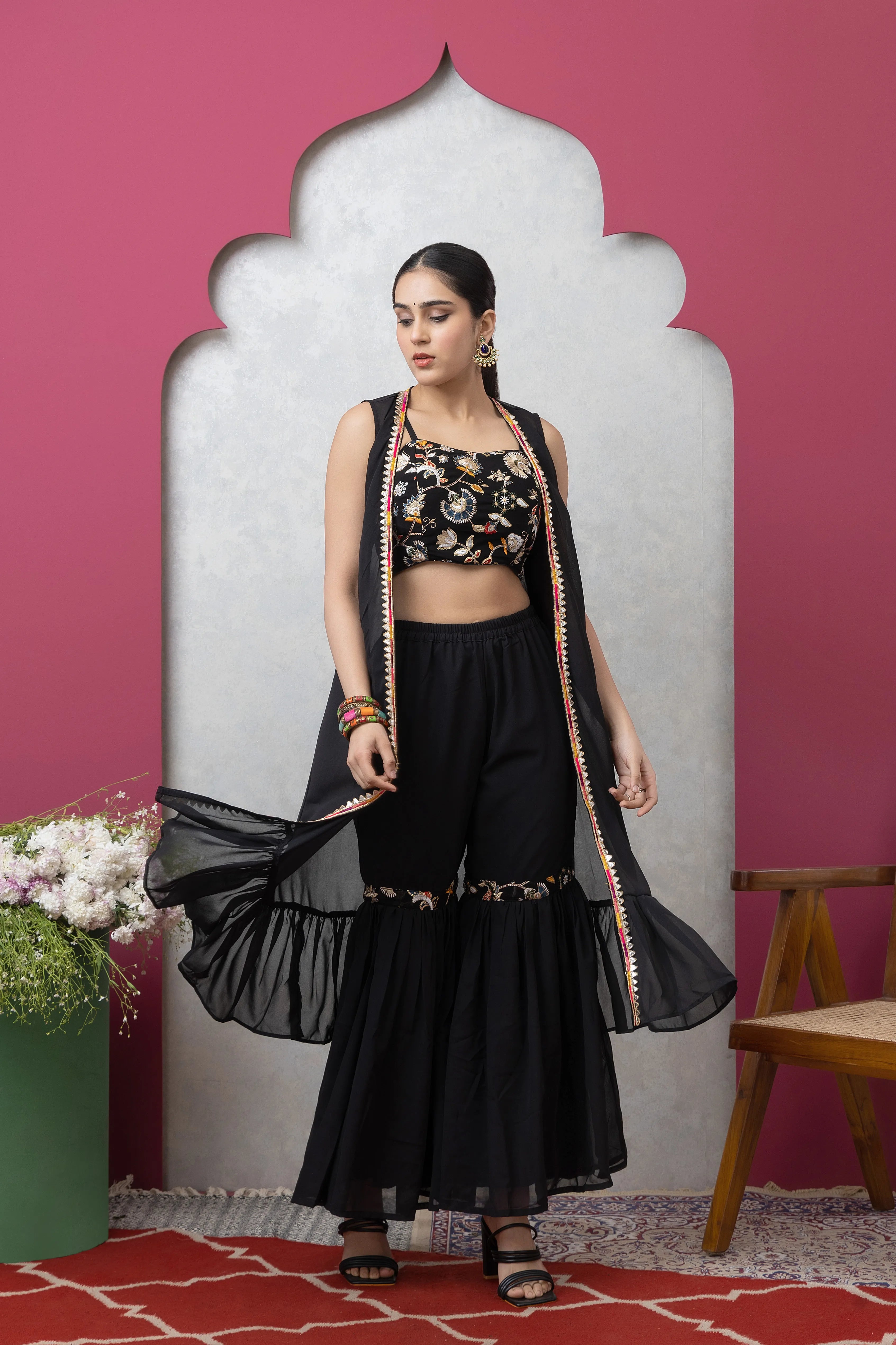 Woman in black traditional outfit with floral top against a pink wall