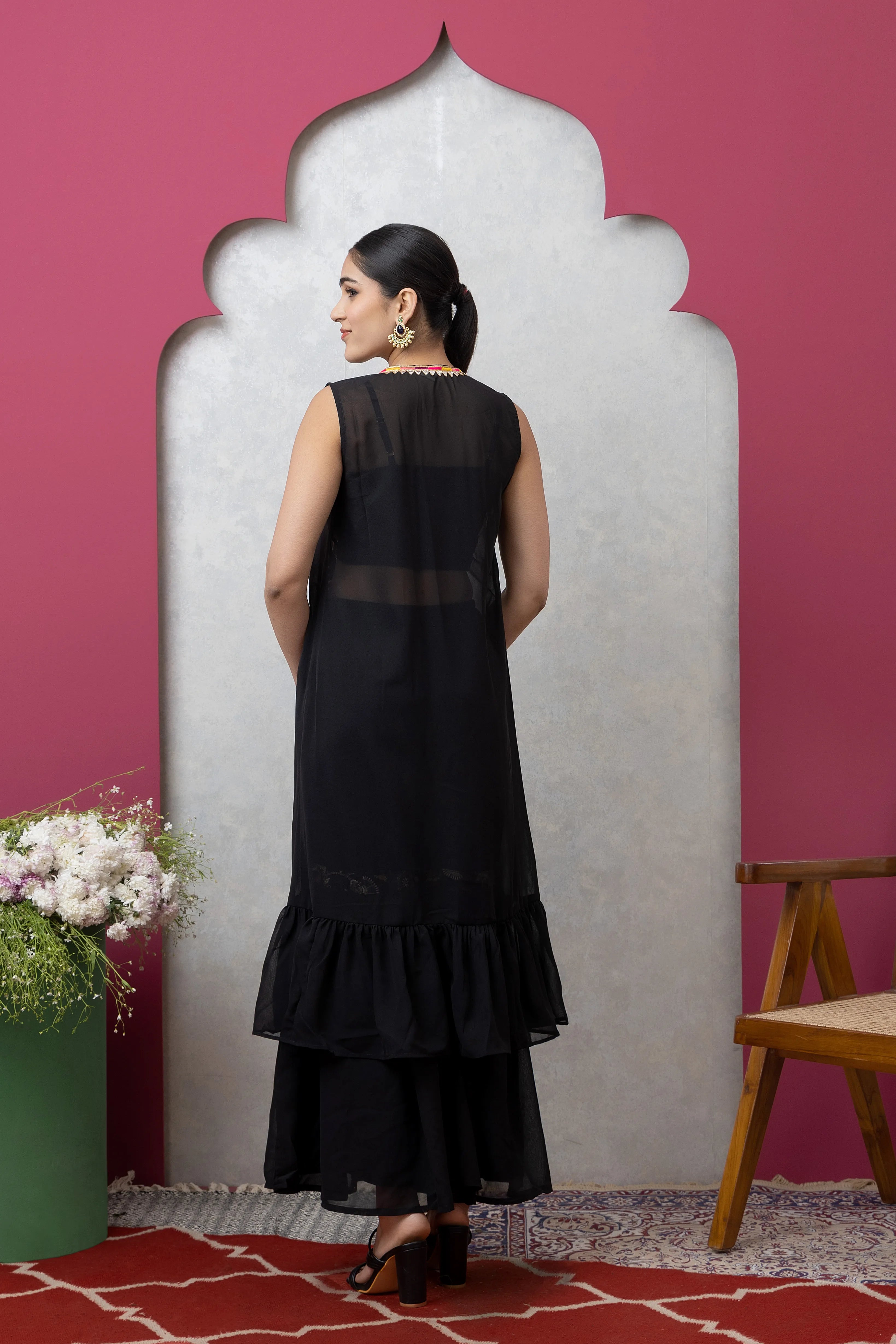 Woman in a black dress standing against a pink wall with a decorative arch.